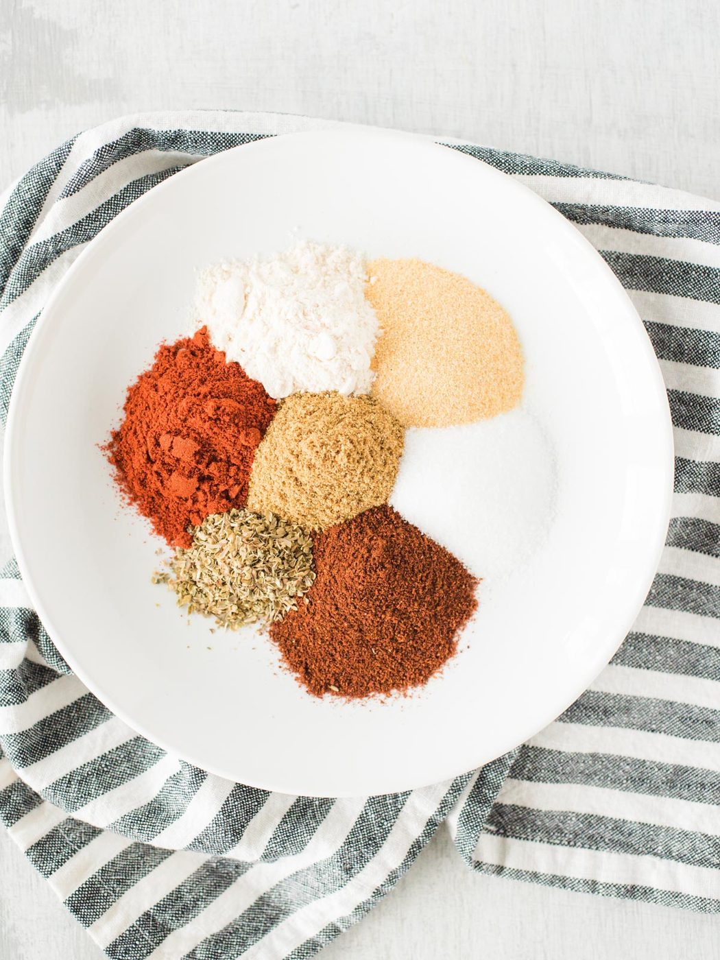 ingredients for taco seasoning on a plate on top of a striped cloth