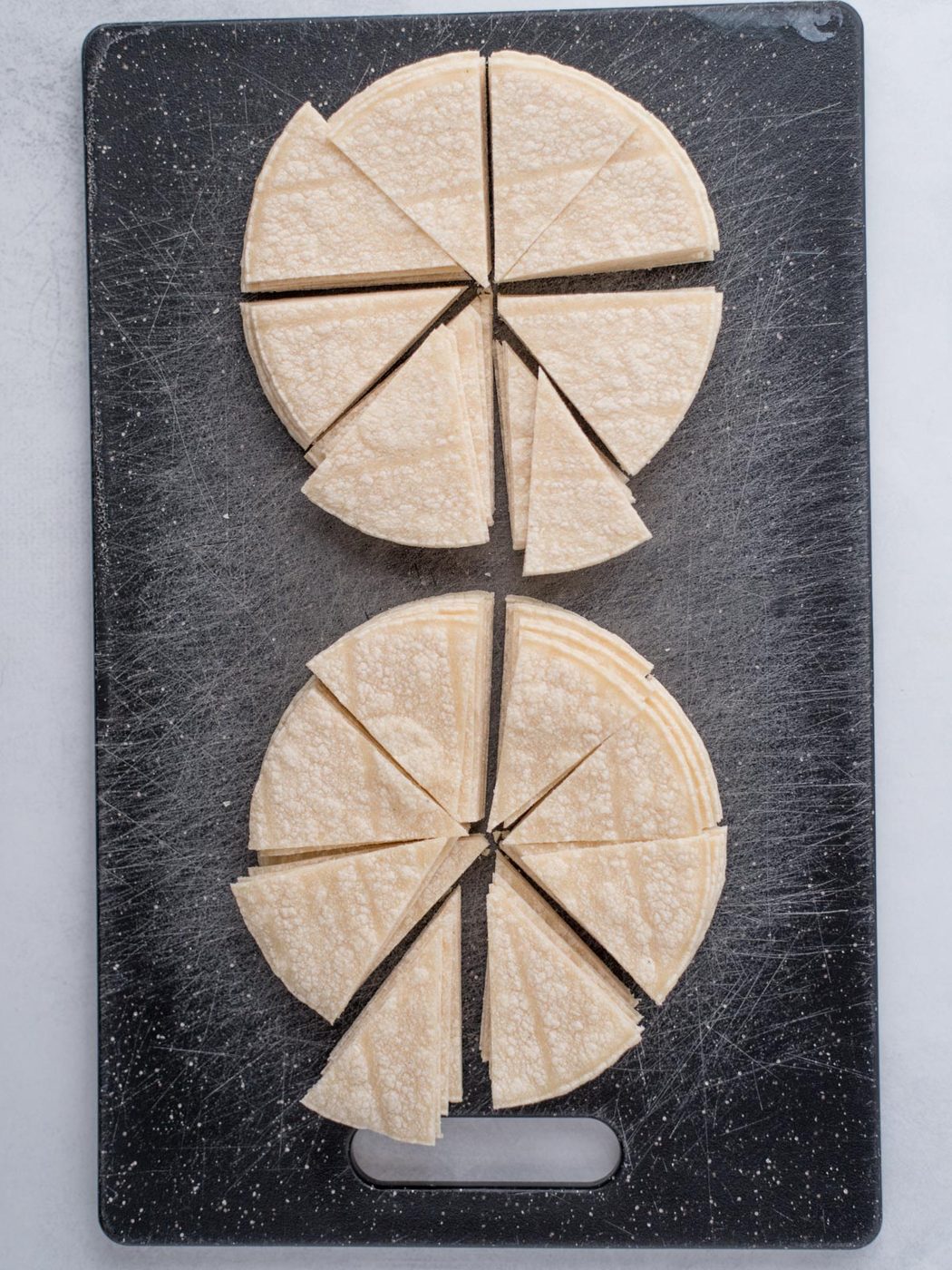 Cutting board with stacks of corn tortillas cut into triangles in preparation for making from-scratch chips.