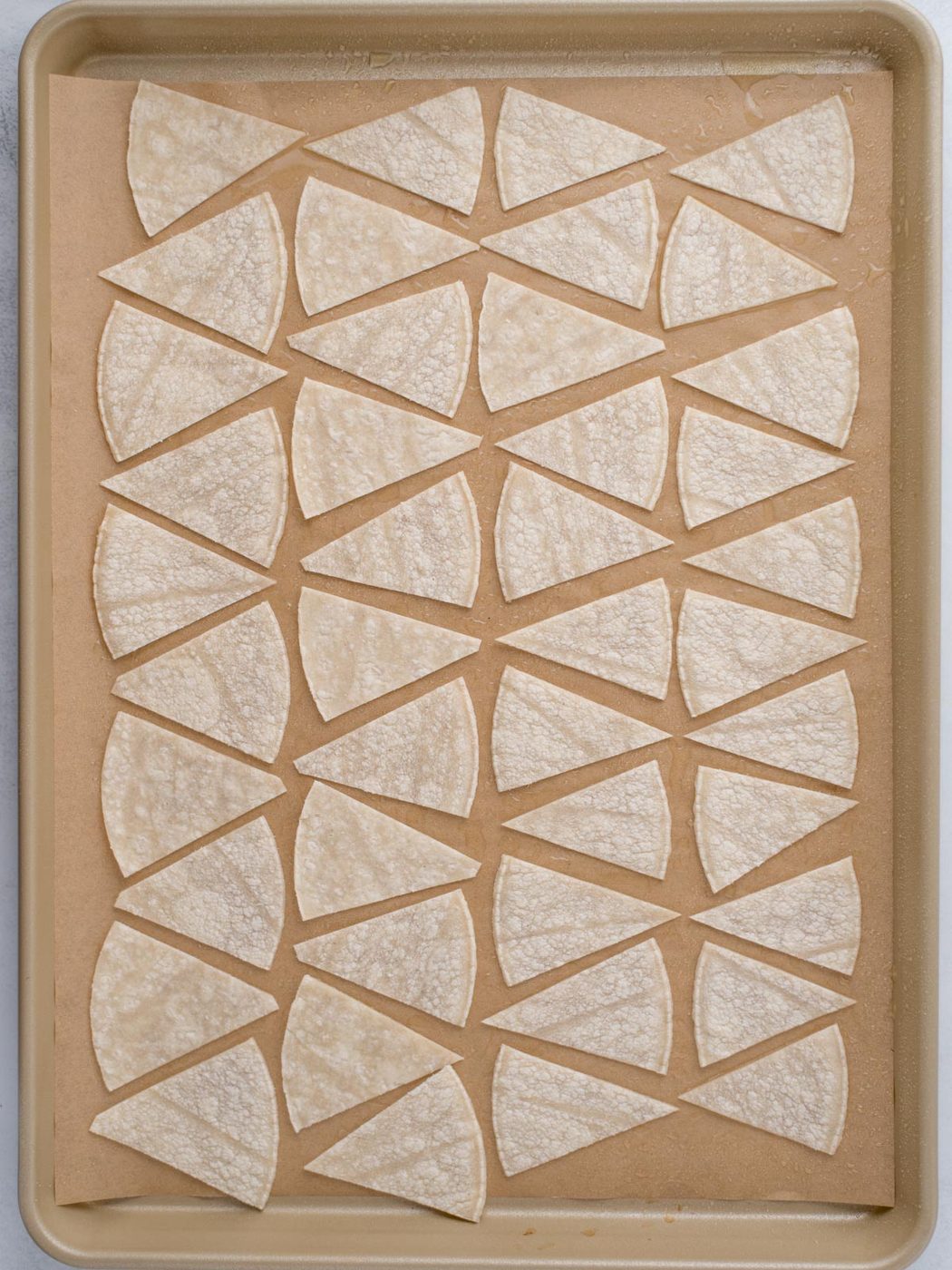 Corn tortillas cut into triangles and arranged on a sheet pan ready to bake.