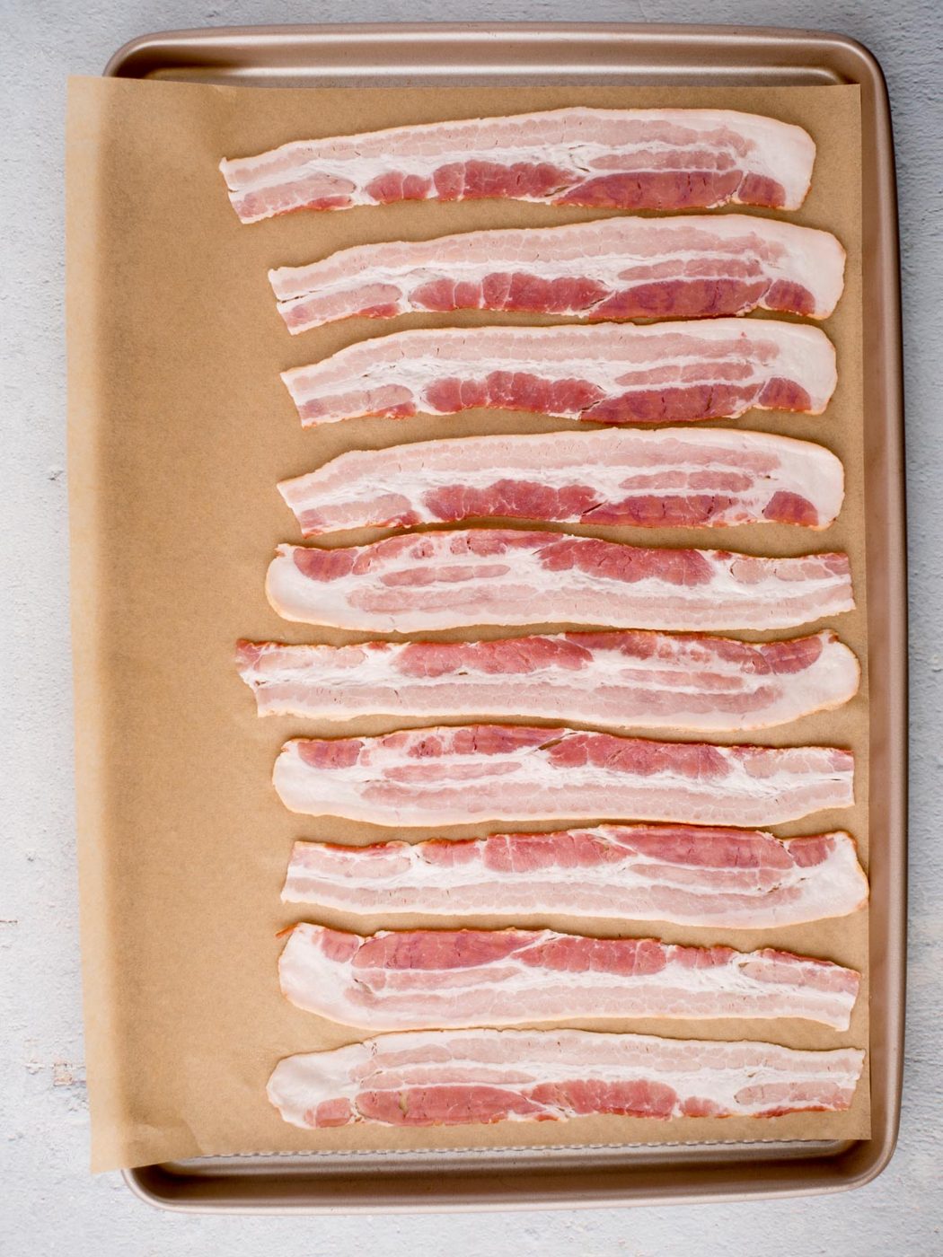 Raw bacon placed in strips on a parchment paper covered baking sheet to prepare honey bacon.