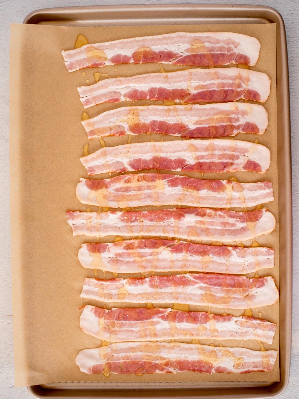 Honey drizzled over bacon strips resting on a parchment paper covered baking sheet.