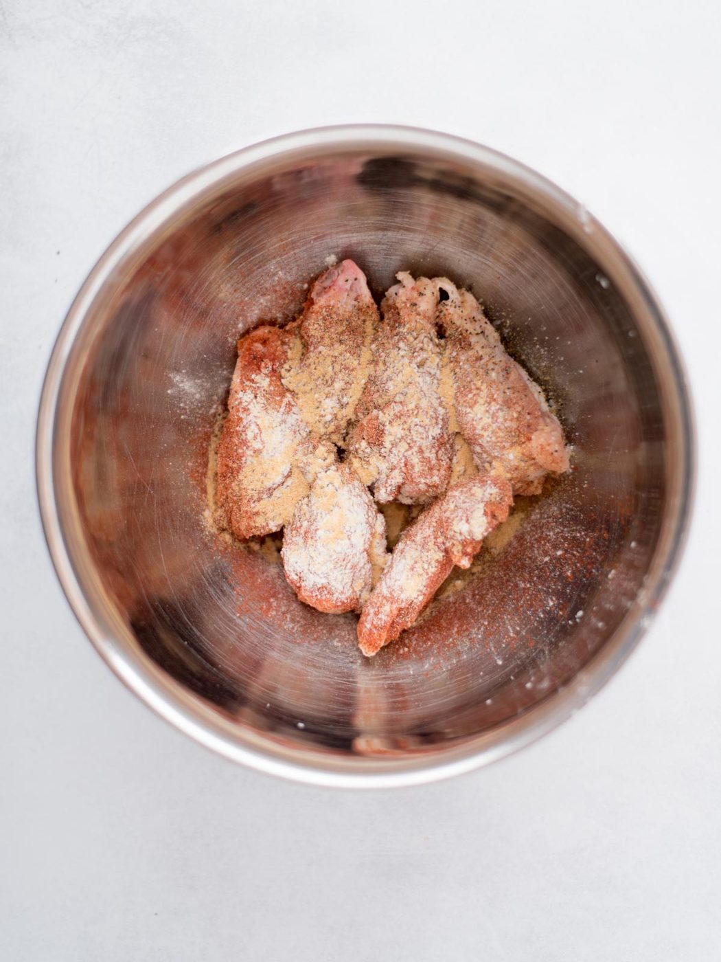 wings in a mixing bowl topped with seasonings