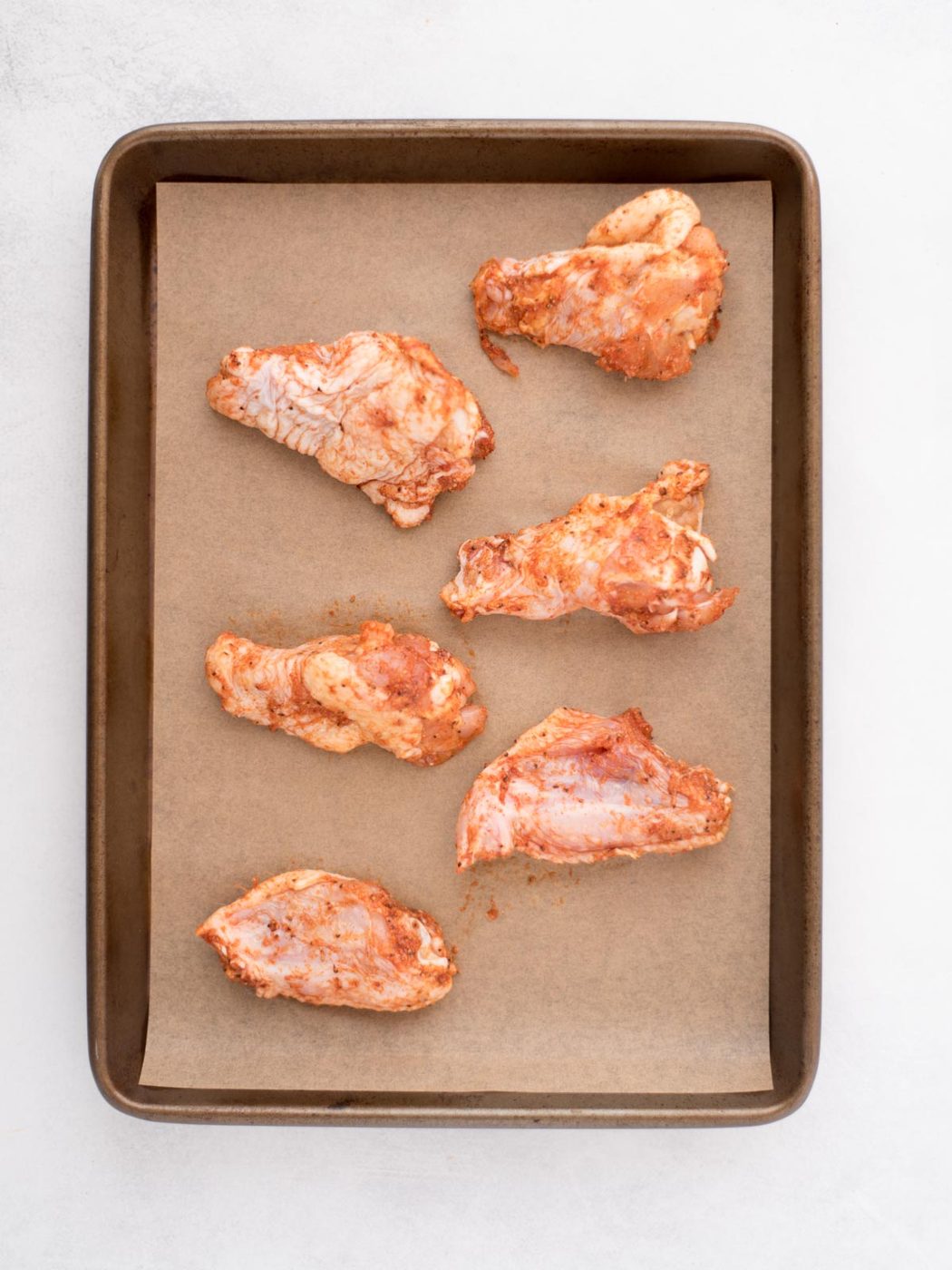 seasoned wings on a parchment lined baking sheet