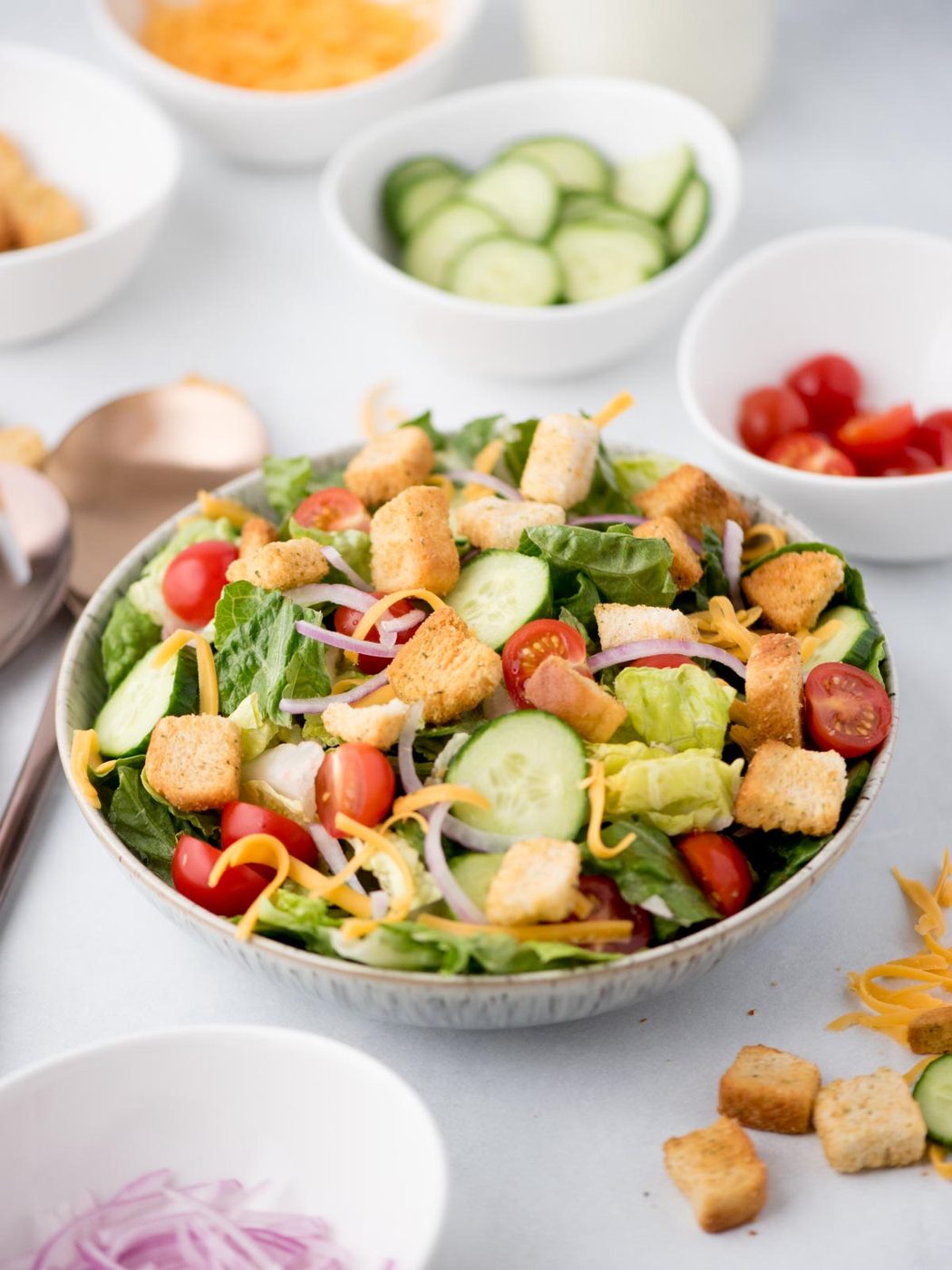 house salad in a bowl surrounded by servings utensils and toppings
