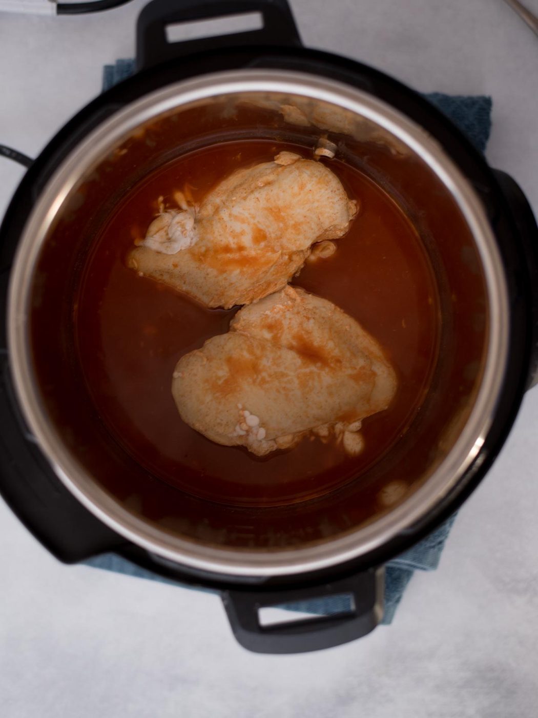 Cooked chicken breasts and buffalo sauce inside the instant pot.
