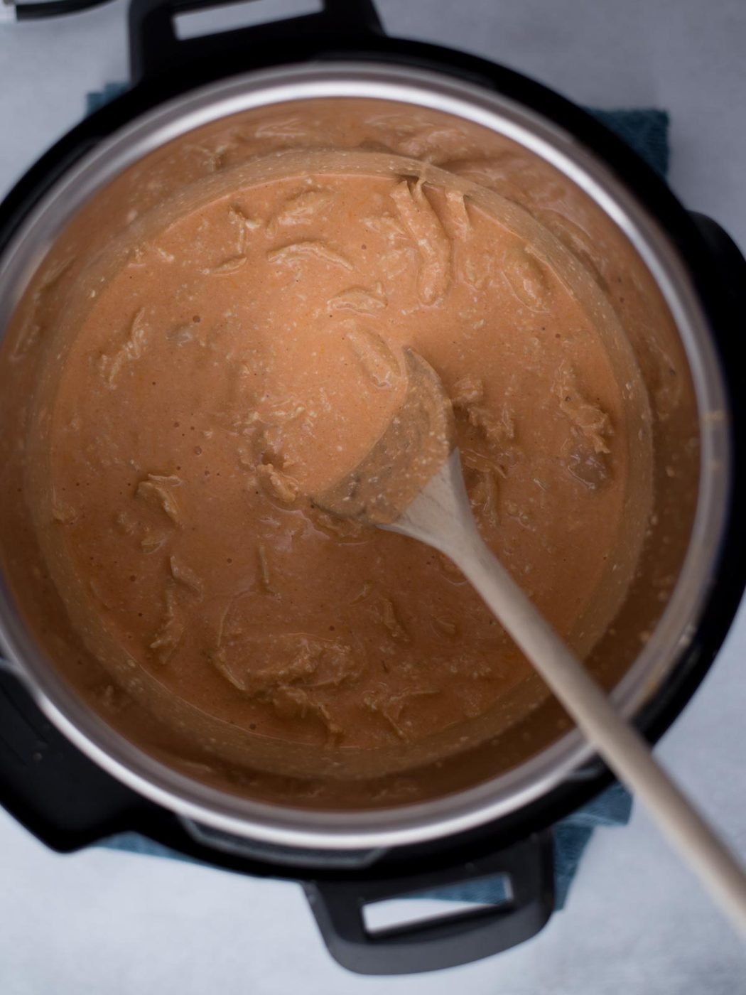 Wooden spoon stirring the creamy buffalo chicken dip inside the instant pot.