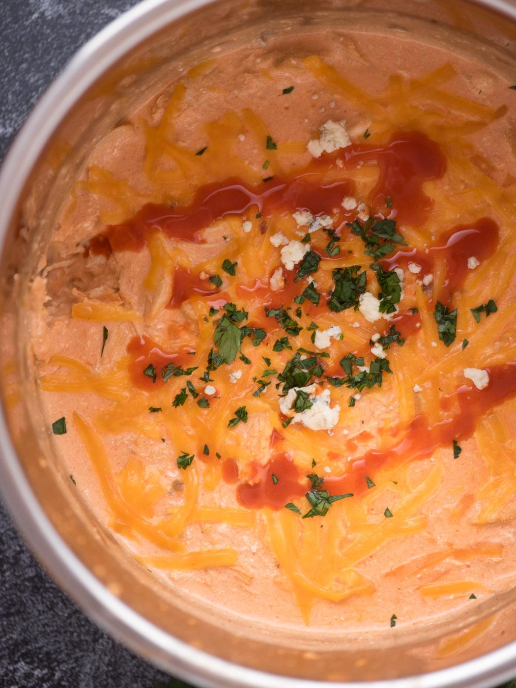 Top view of Buffalo Chicken Dip in a bowl with buffalo sauce drizzled over the top with chopped cilantro and cheese crumbles.