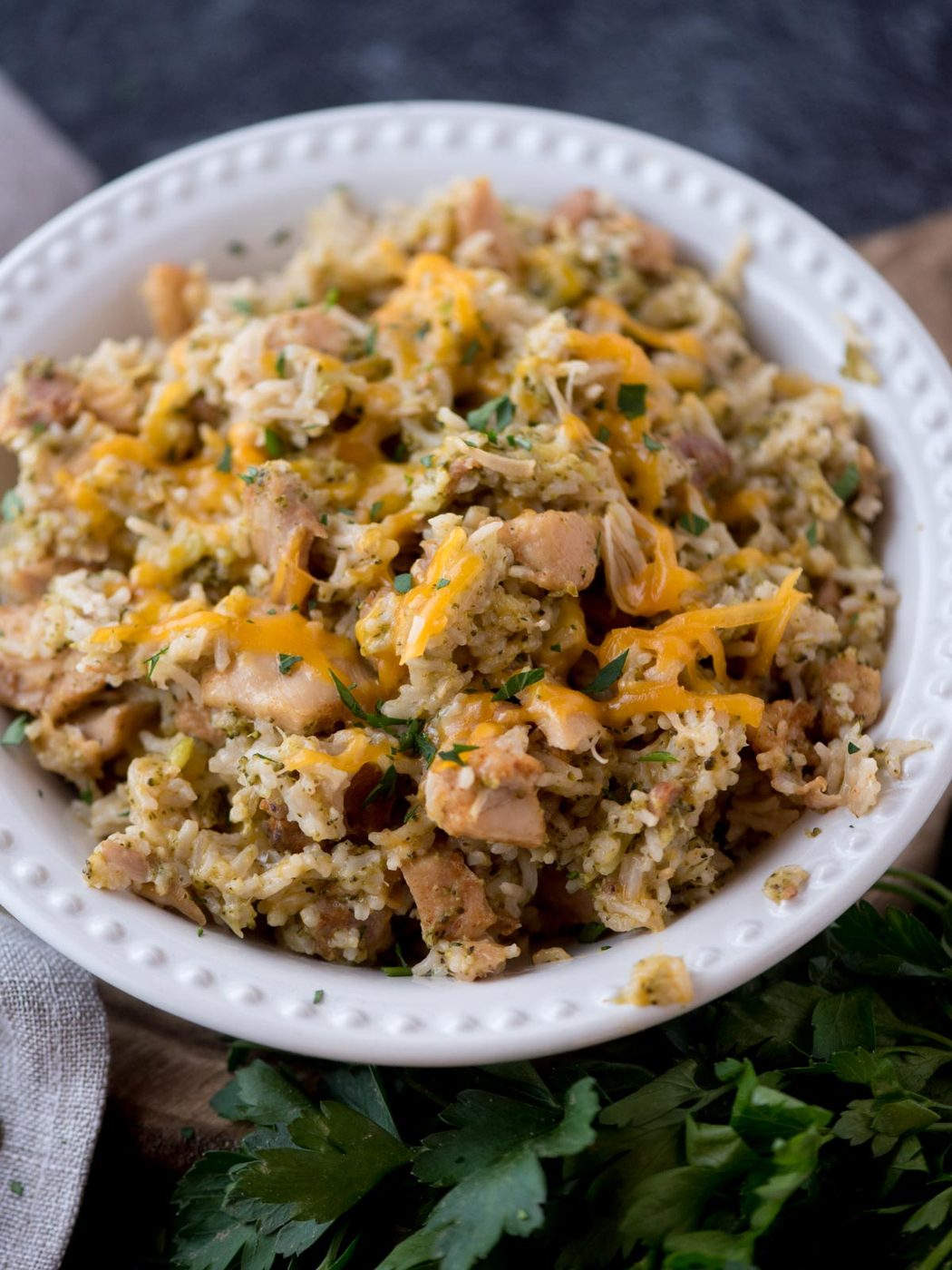 instant pot chicken broccoli rice casserole in a white bowl topped with cheese and surrounded by fresh parsley
