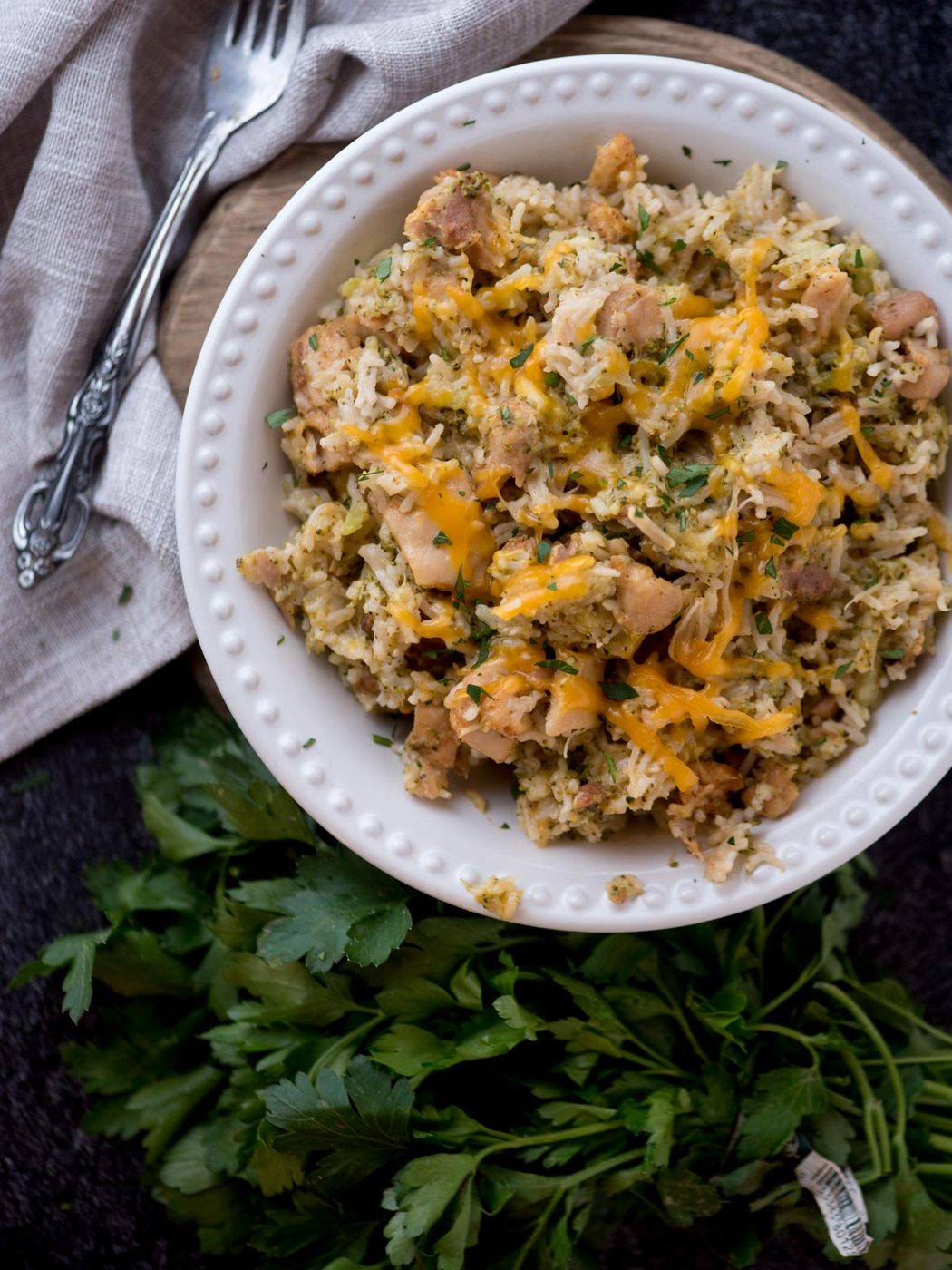 instant pot chicken broccoli rice in a white bowl topped with cheese and surrounded by fresh parsley