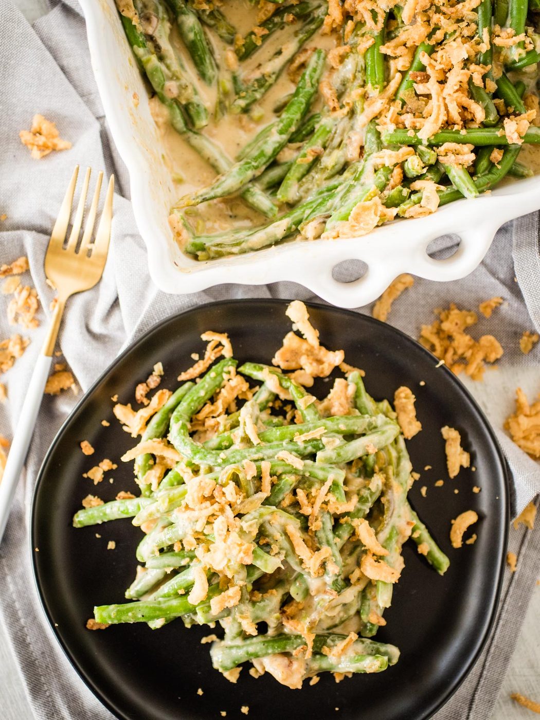 a serving of green bean casserole on a black dish next to the serving dish full of casserole