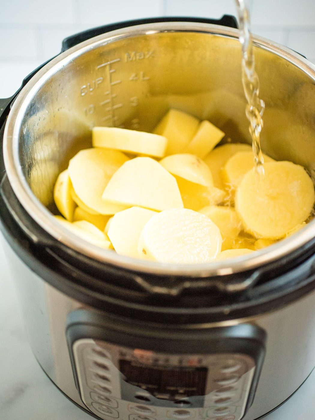 sliced potatoes in an instant pot with water pouring over them