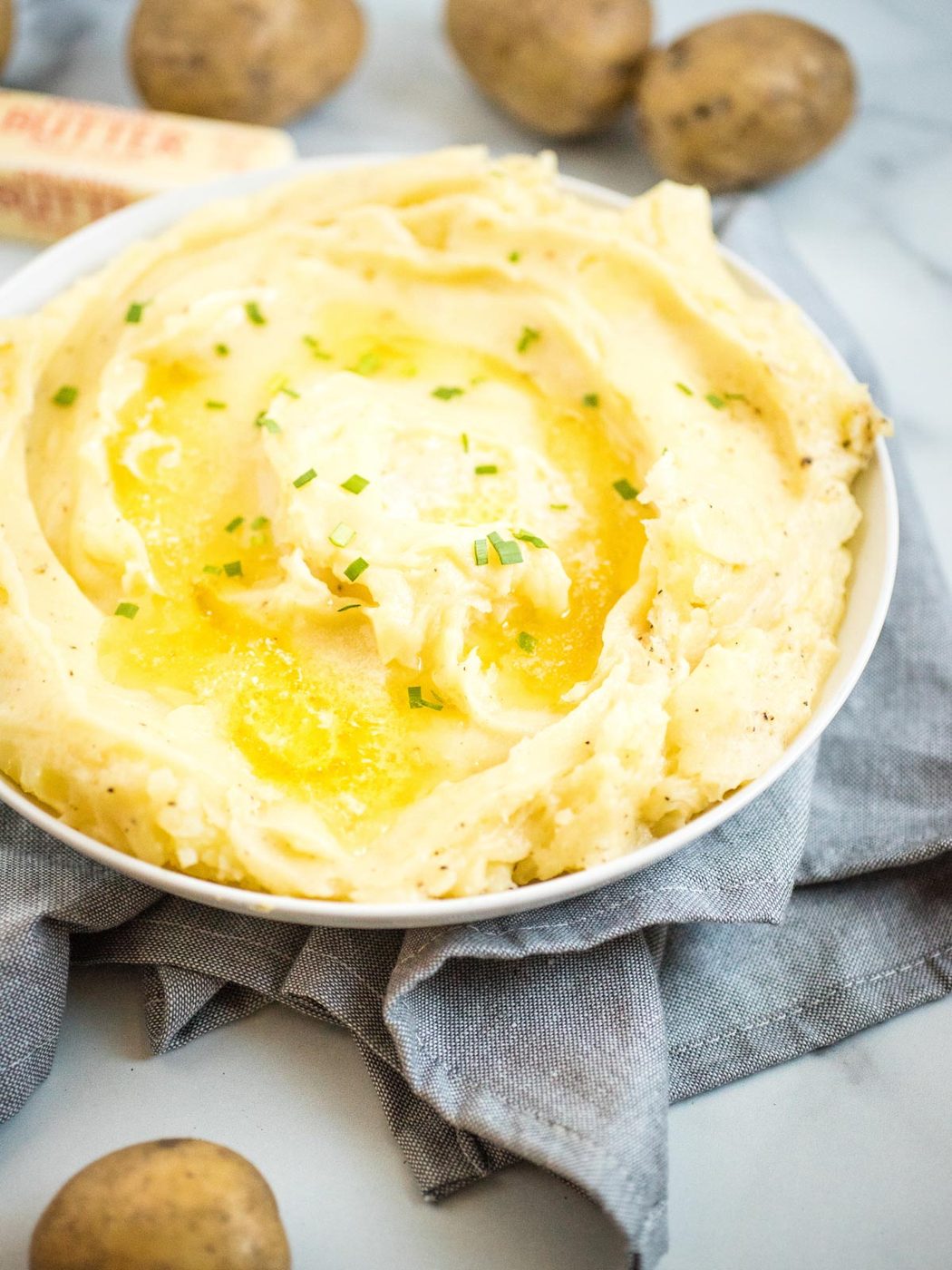 mashed potatoes in white dish topped with melted butter and chives