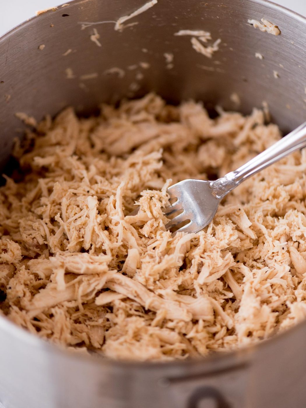 A metal fork shredding cooked chicken in a large stainless steel pot, creating tender instant pot shredded chicken breast.