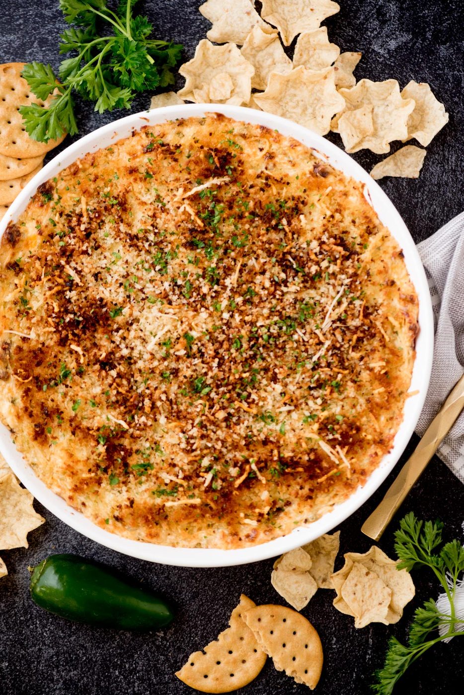 jalapeno popper dip in a white baking dish surrounded by crackers, chips, jalapenos, and parsley