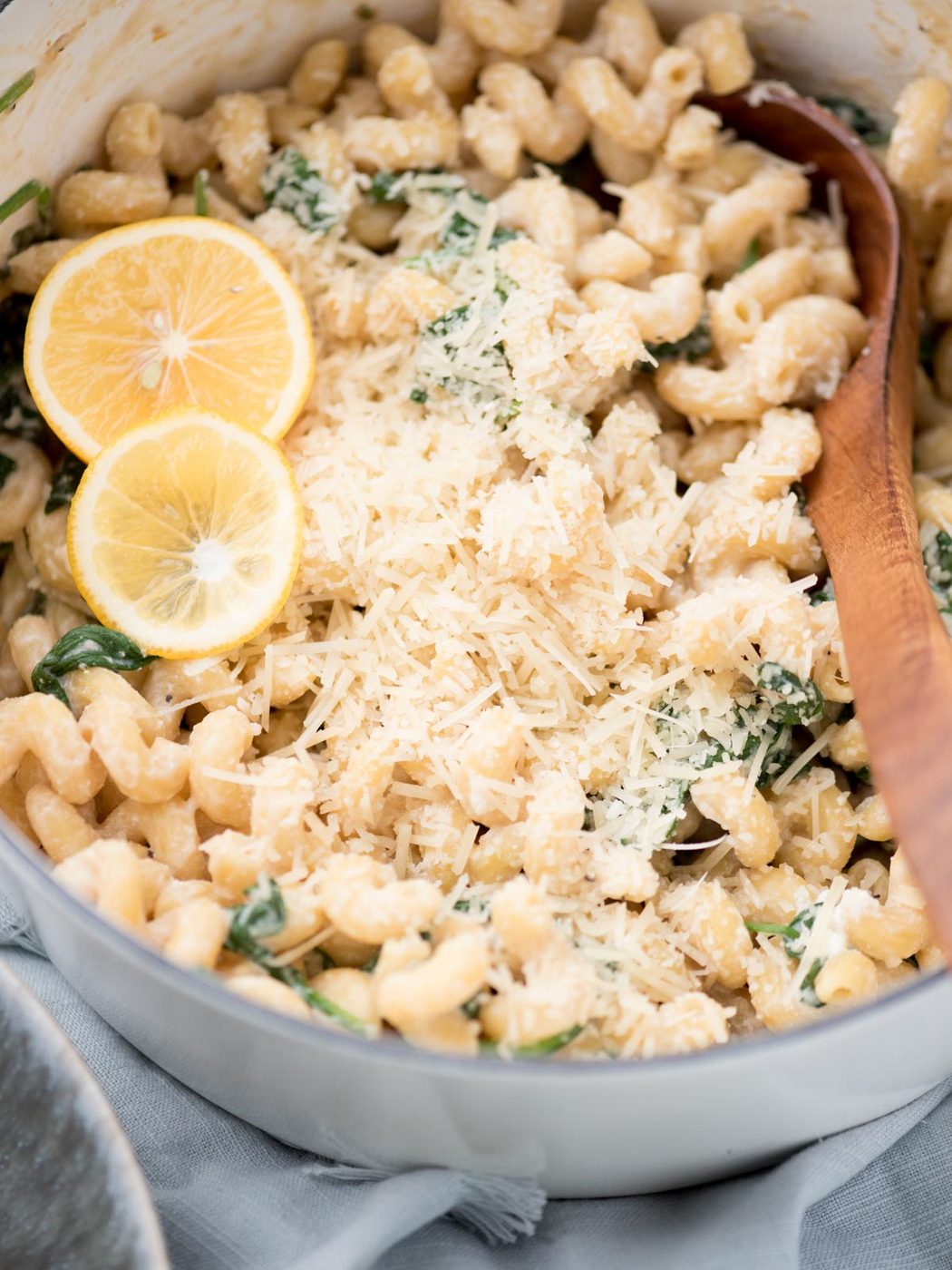 Wooden spoon in the dutch oven lemon ricotta pasta with lemon slices on top.