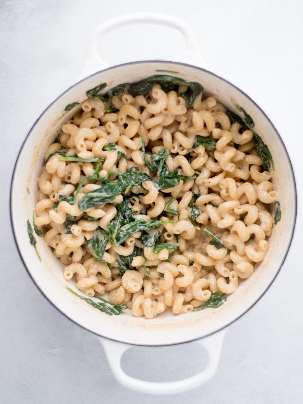 Cooked pasta mixed with wilted spinach in a dutch oven.