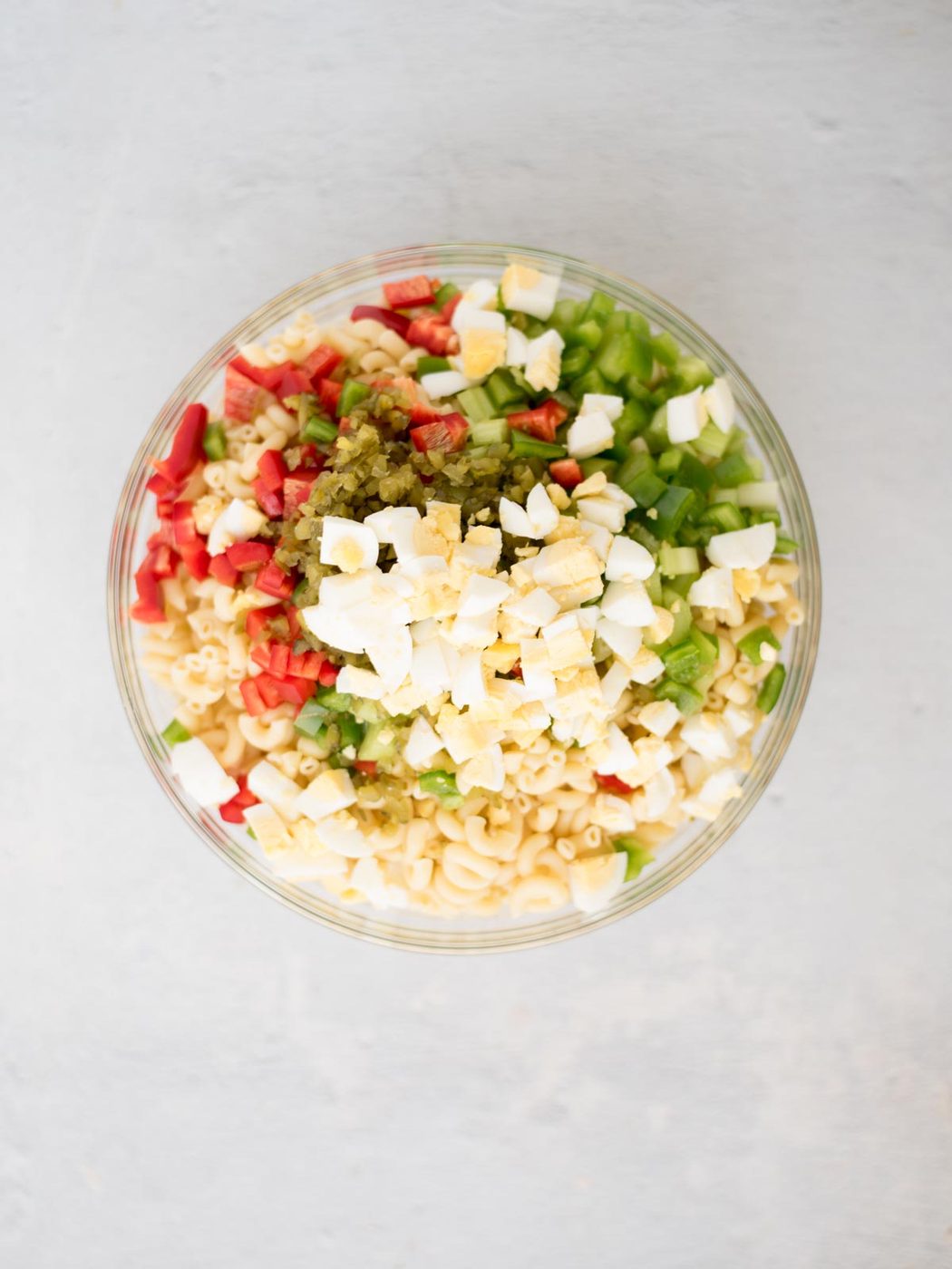 All of the ingredients for southern macaroni salad in a glass mixing bowl before it's been mixed together.
