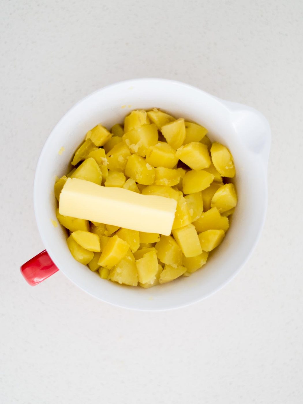 Mixing bowl with cut up cooked potatoes and a stick of butter added to the top.