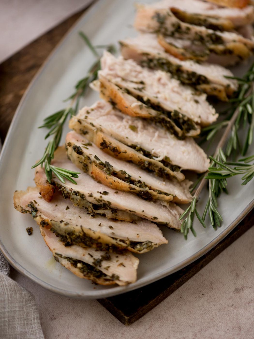 slices of oven roasted turkey on a ceramic platter surrounded by fresh rosemary sprigs