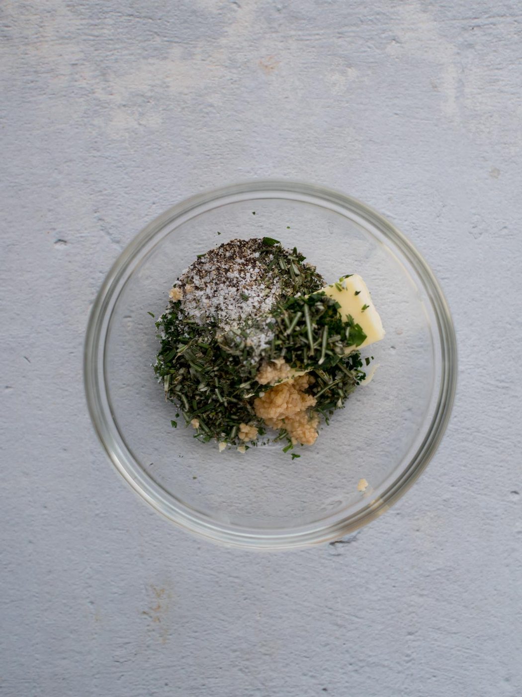 ingredients for herbed butter in a glass mixing bowl