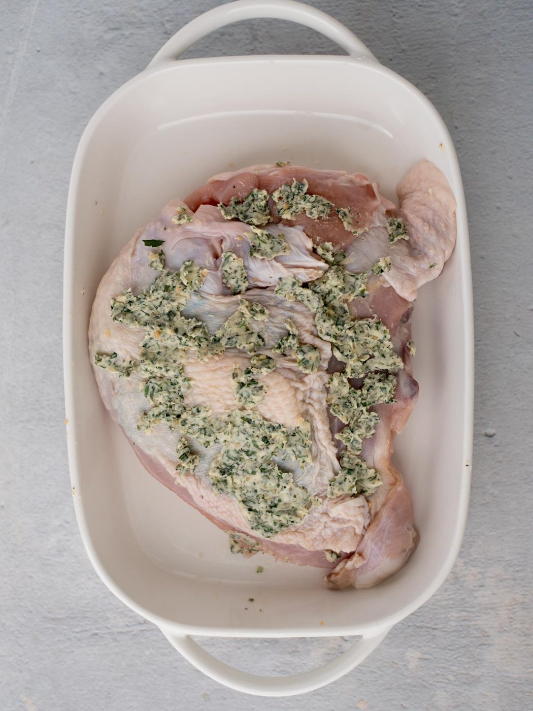 raw turkey breast in a casserole dish covered in herbed butter