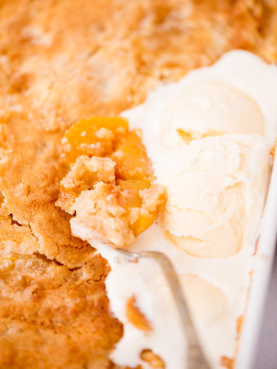 Close up of a spoon scooping up peach cobbler with ice cream.