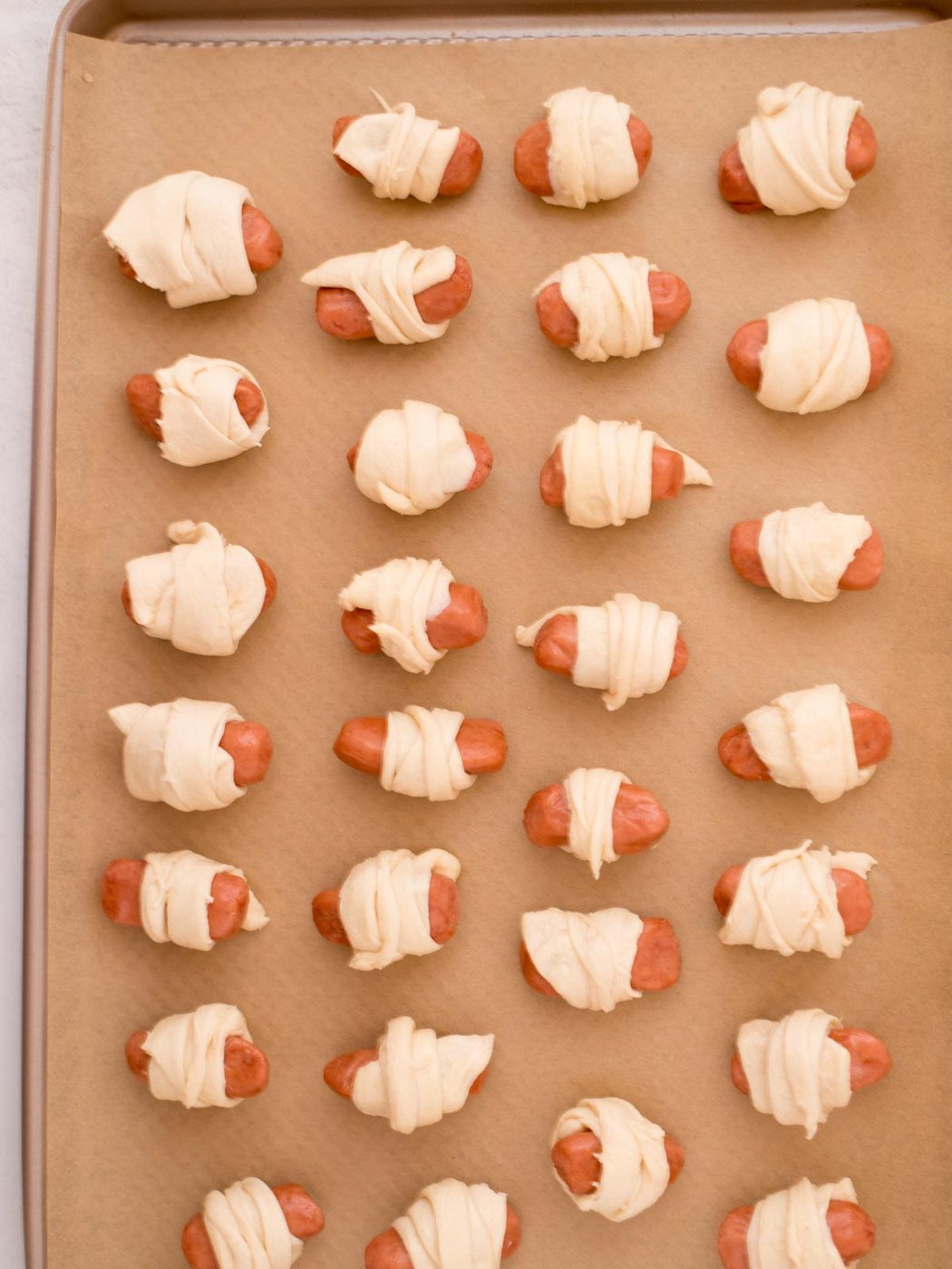 Lil smokie sausages wrapped in crescent roll dough on a parchment paper covered baking sheet.