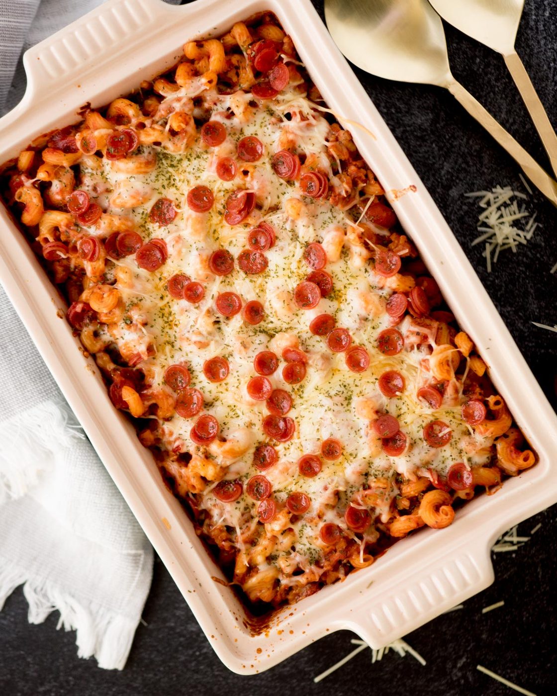 pizza casserole in a baking dish surrounded by a kitchen towel and servings utensils