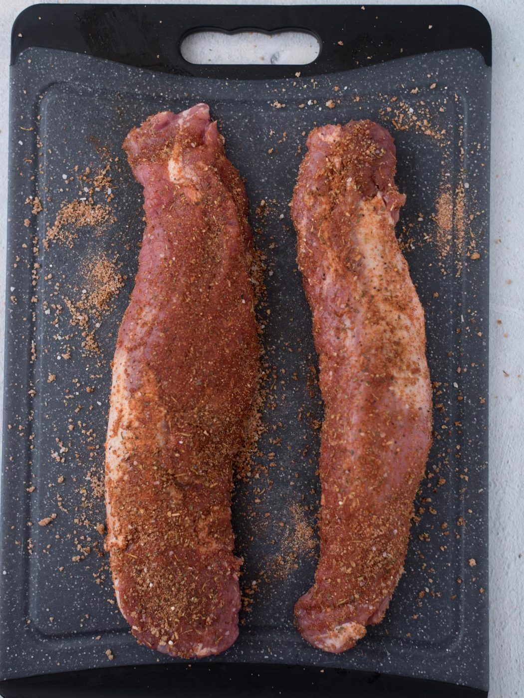 seasoned raw pork tenderloin on a black cutting board