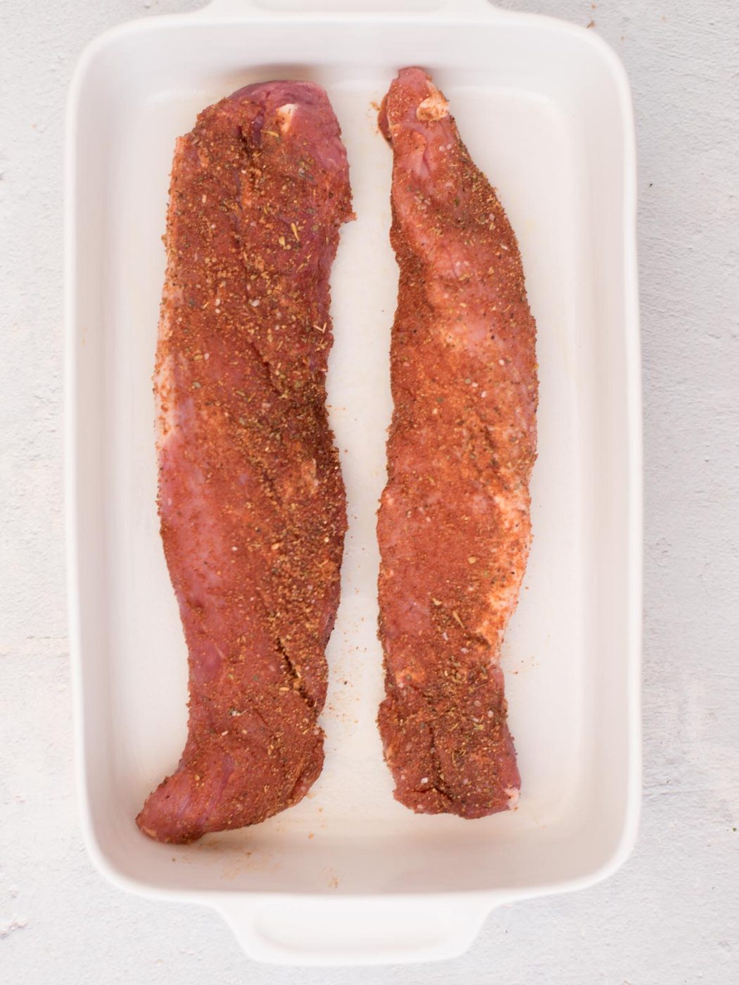 seasoned raw pork tenderloin in a white baking dish