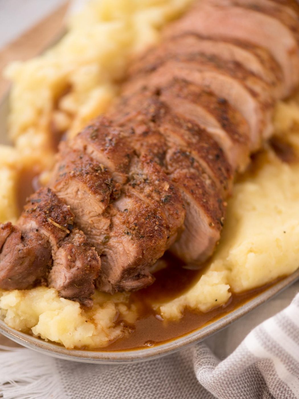 sliced pork tenderloin on top of mashed potatoes in a serving platter