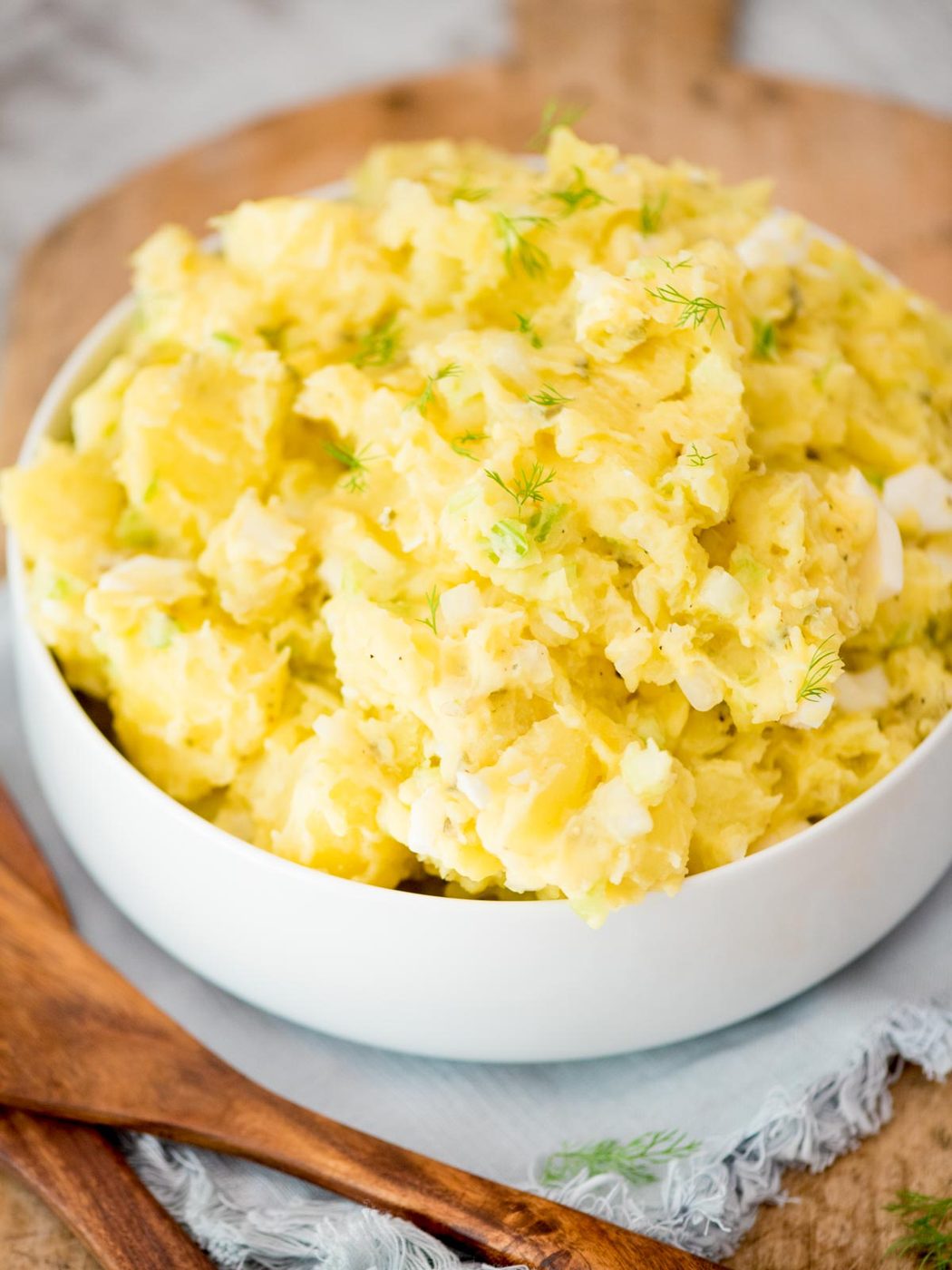potato salad topped with fresh dill in a white bowl