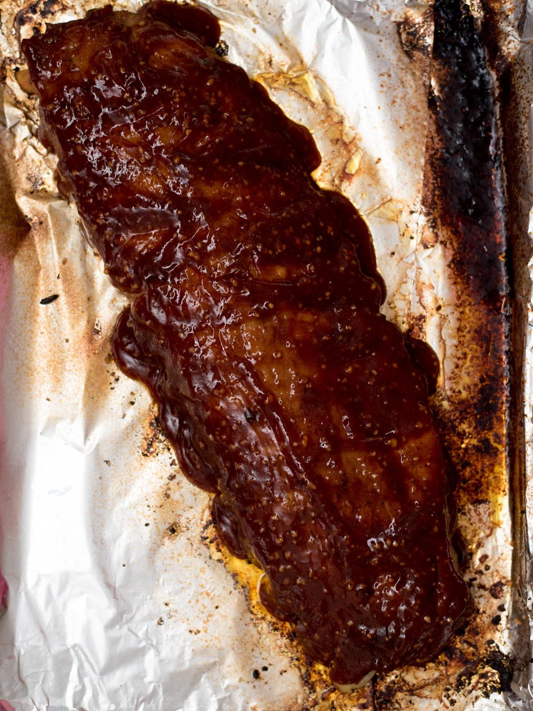 Freshly baked ribs in the oven laying on a foil covered baking sheet with sauce coating the top.