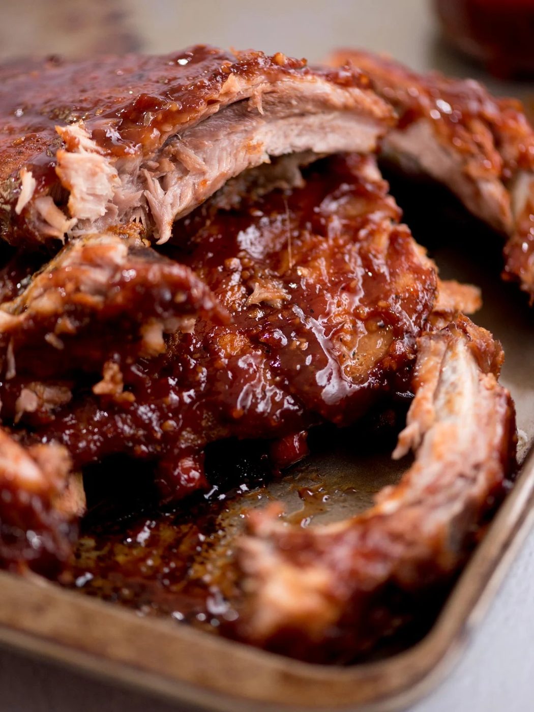 Saucy ribs on a baking sheet with a few ribs pulled away to show the tender meat.