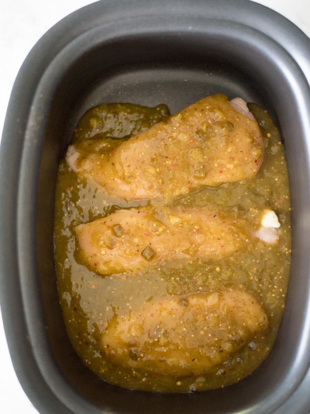 Seasoned chicken in the crockpot covered in salsa verde.