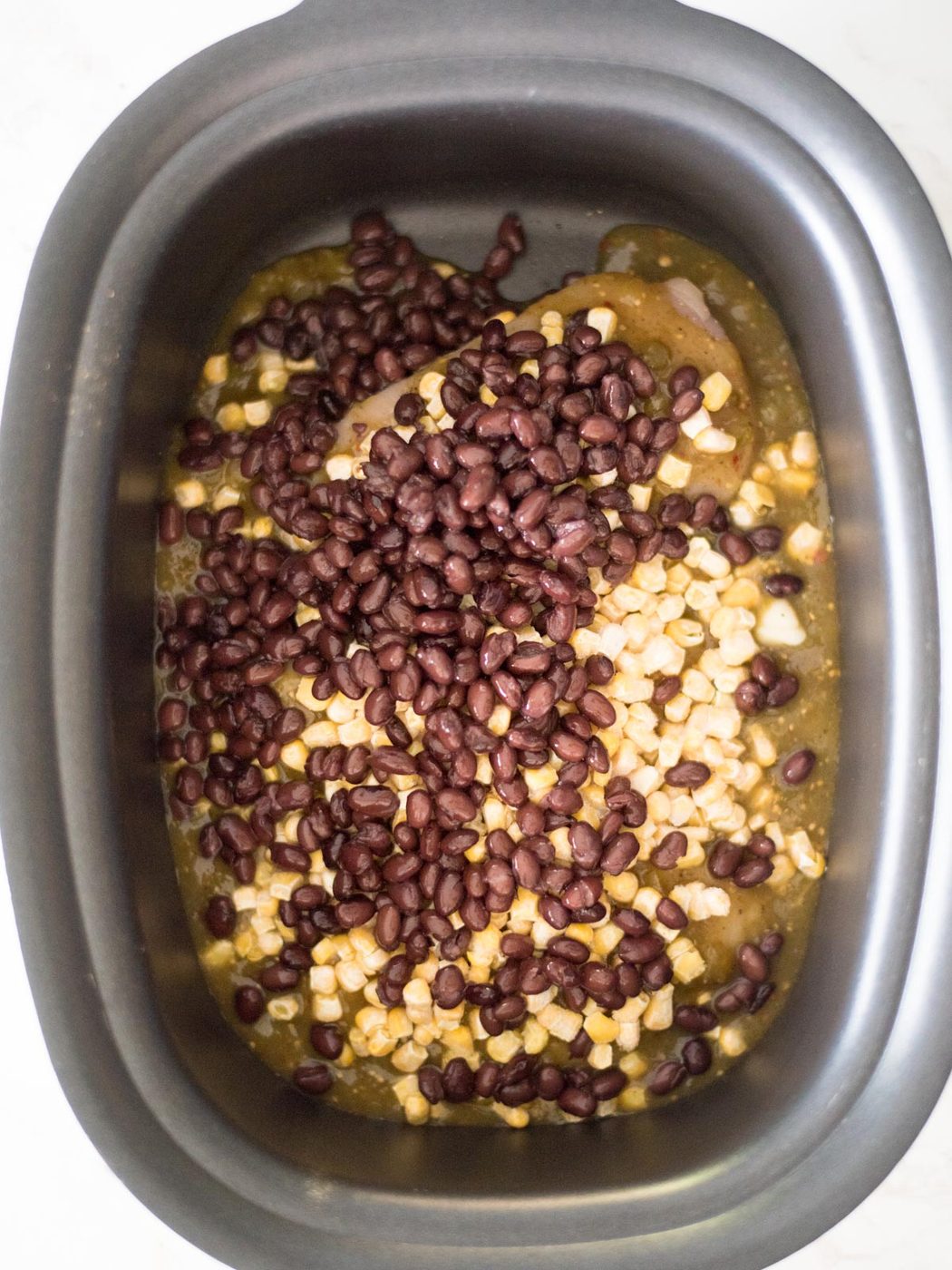 Black beans added to the crockpot with the chicken, corn, and salsa verde.