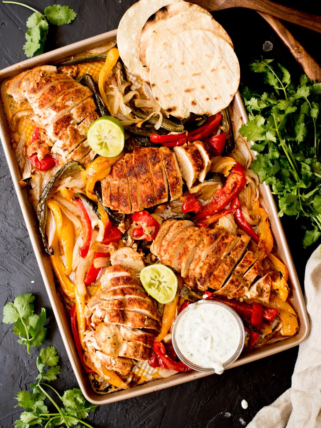 sheet pan chicken fajitas with creamy cilantro lime sauce, tortillas, and limes