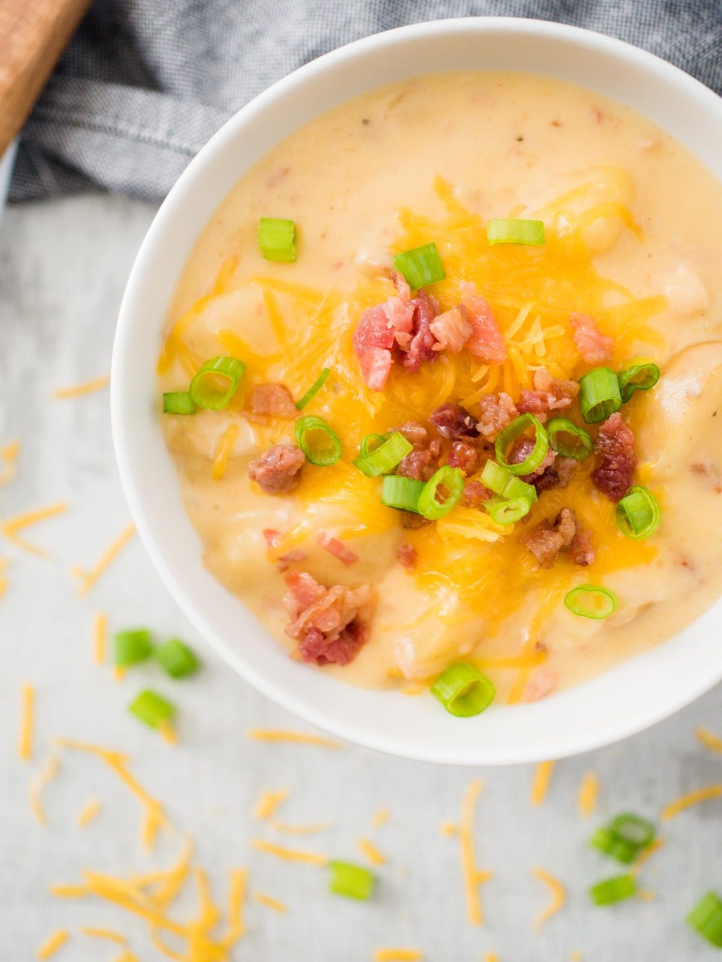 slow cooker potato soup in white bowl with toppings of cheese and scallion