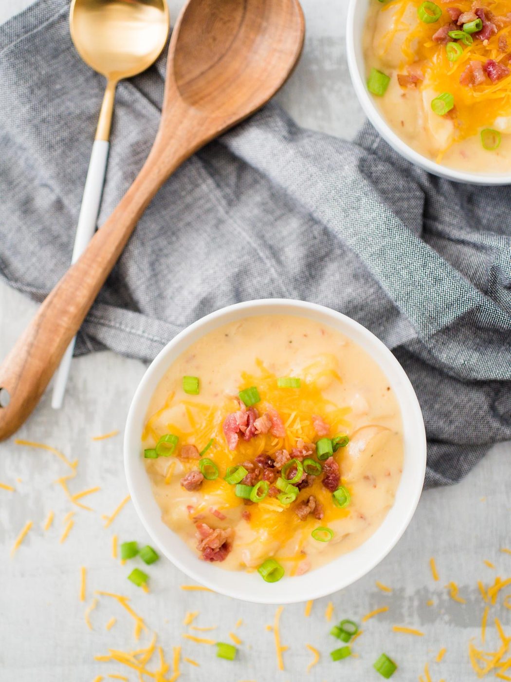 slow cooker potato soup in white bowl with toppings of cheese and scallion