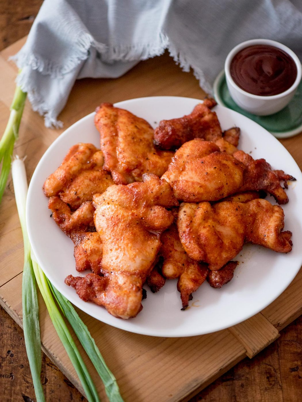 Green onions laying next to a plate of smoked chicken thighs.