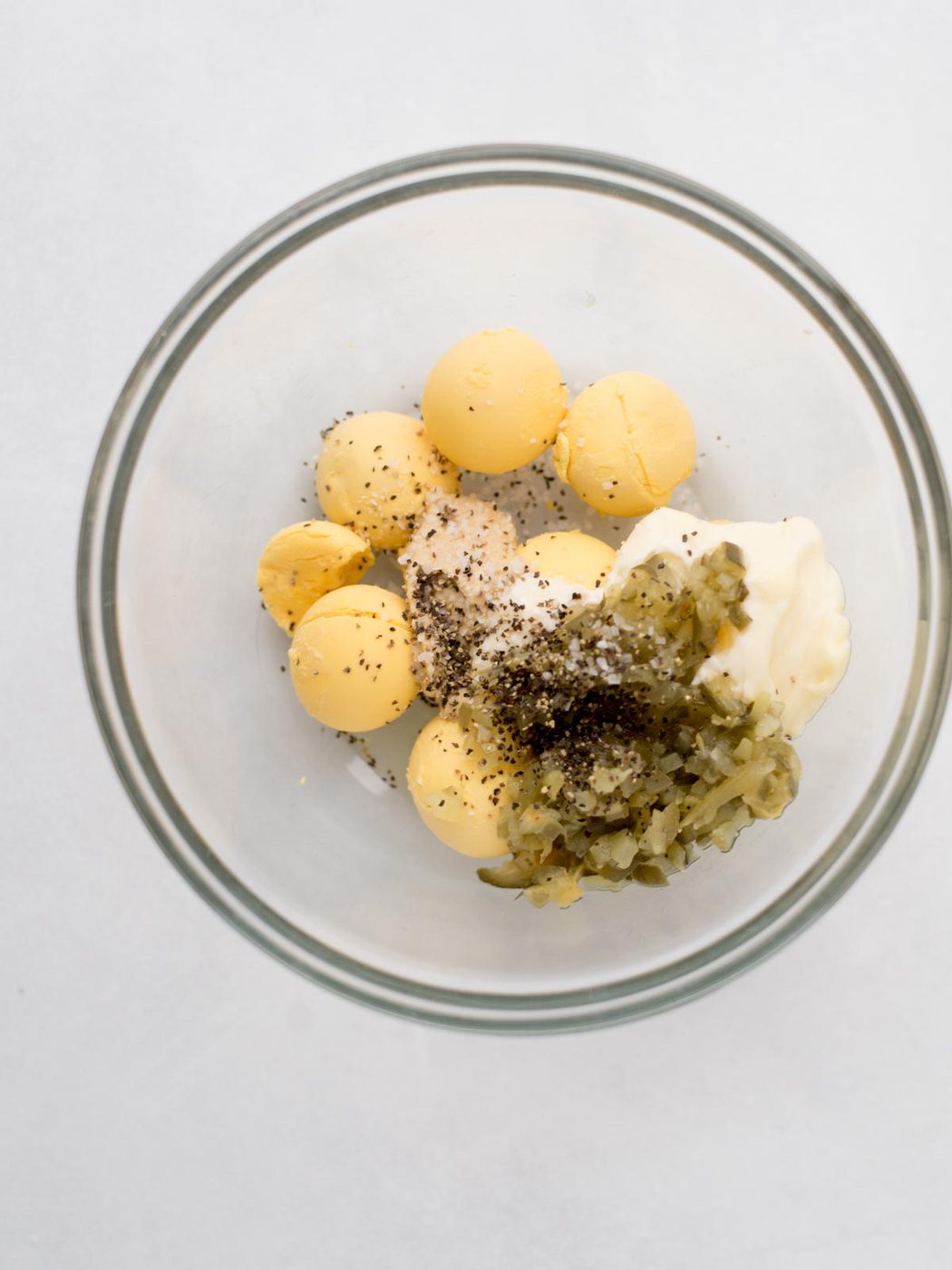 cooked egg yolks, with relish, seasoning and mayo in a mixing bowl, ready to combine.
