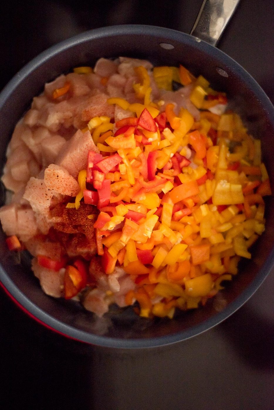 Chopped bell pepper, taco seasoning, and chicken in a skillet on the stove.