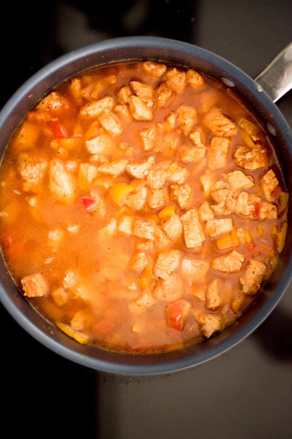 Liquid added to the skillet with the chicken, rice, and bell peppers on the stove.