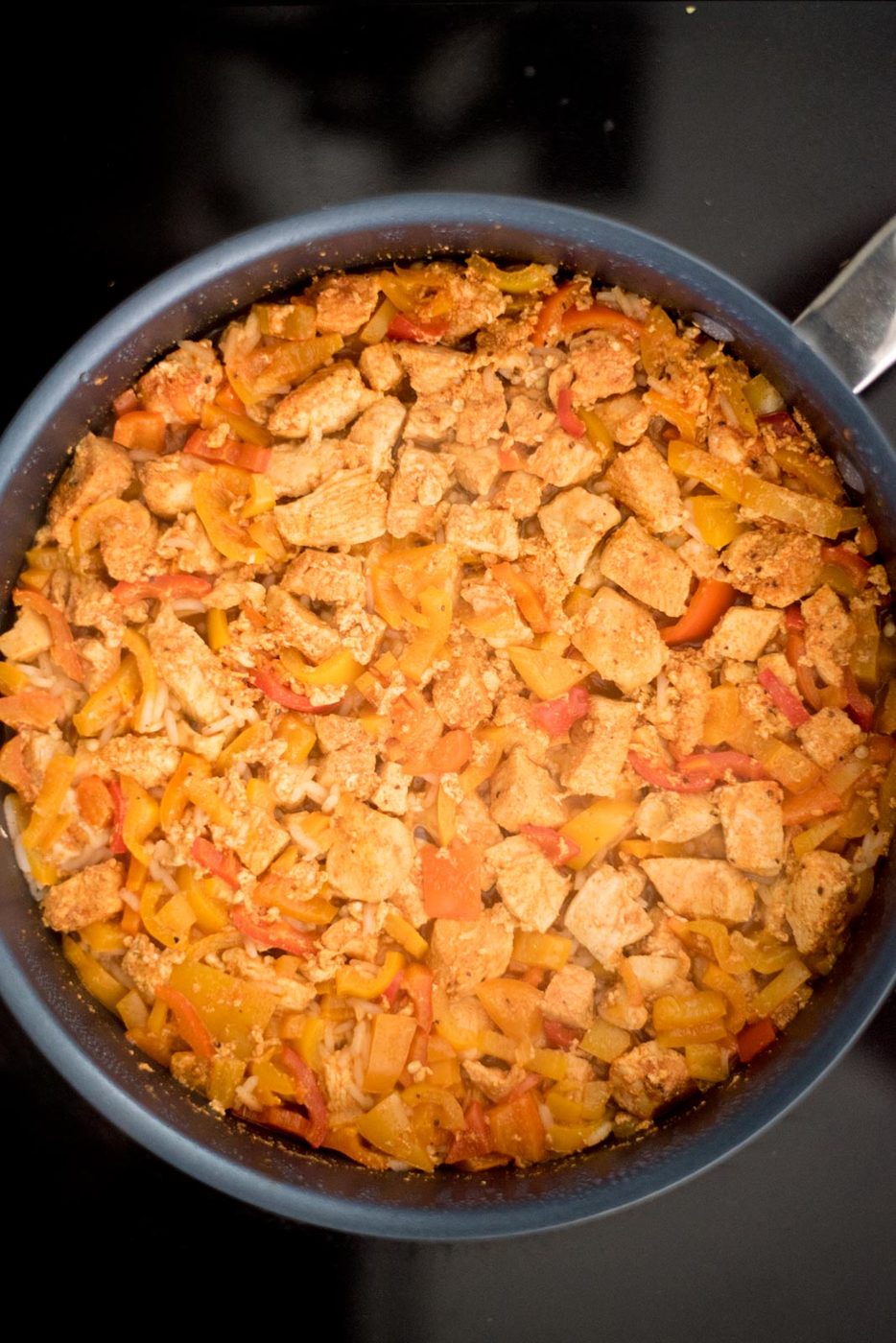 Cooked chicken, bell peppers, and rice in a skillet on the stove.