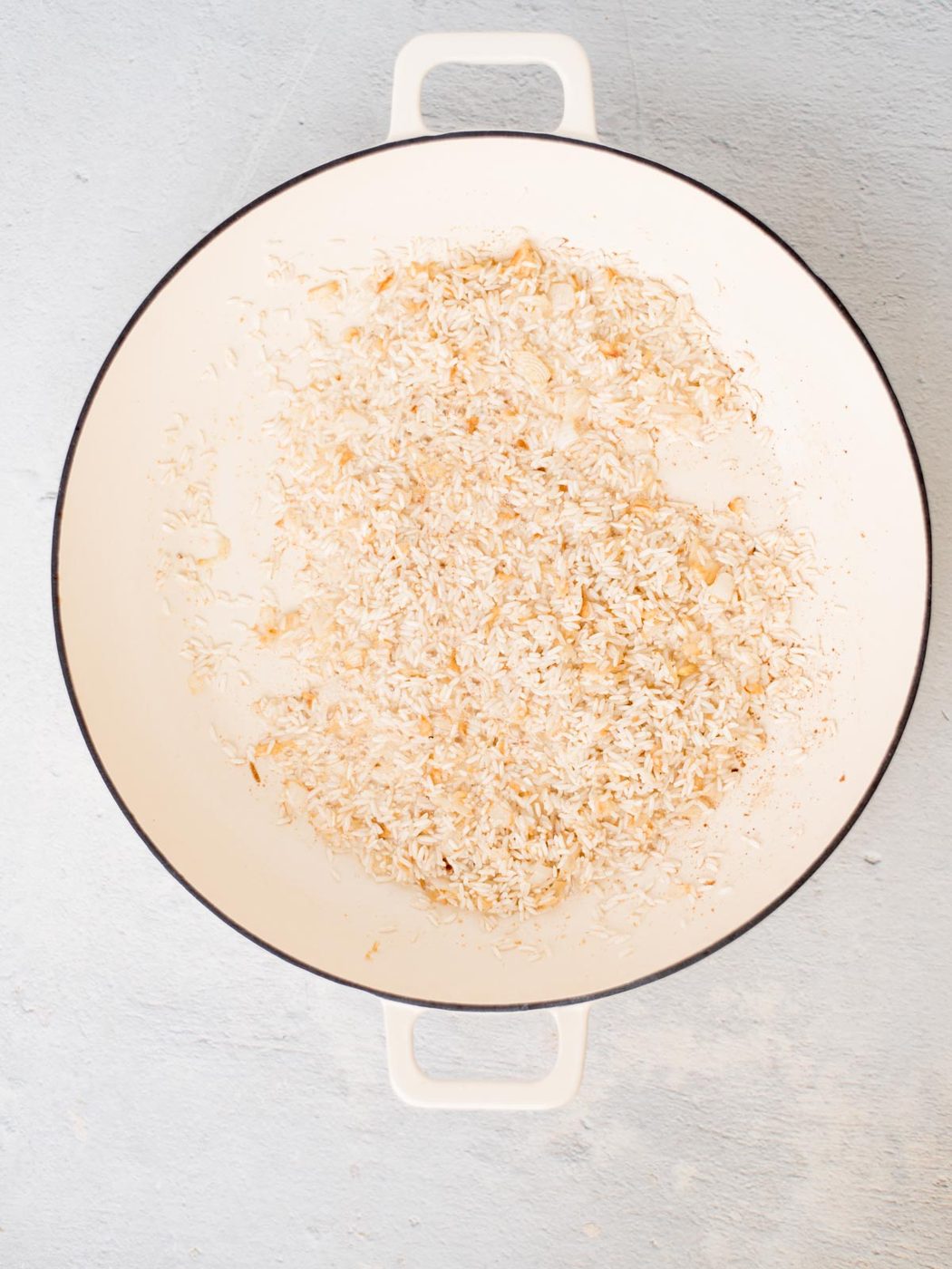 rice toasting with oil, onion, and garlic powder in a white skillet