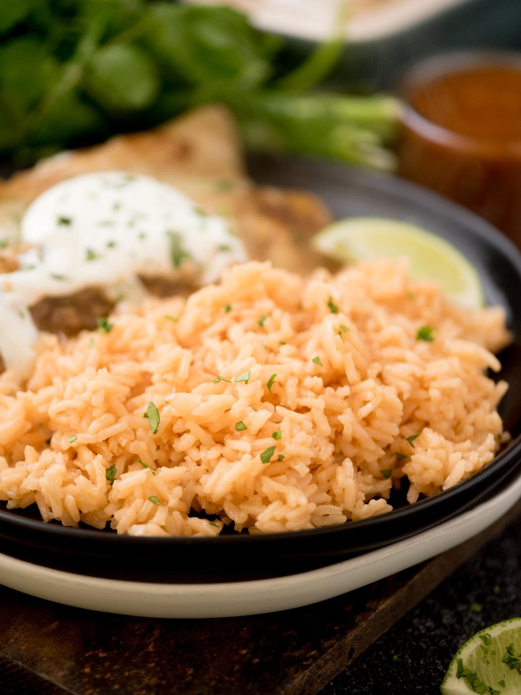 spanish rice on a plate with enchiladas topped with chopped cilantro on a wooden board