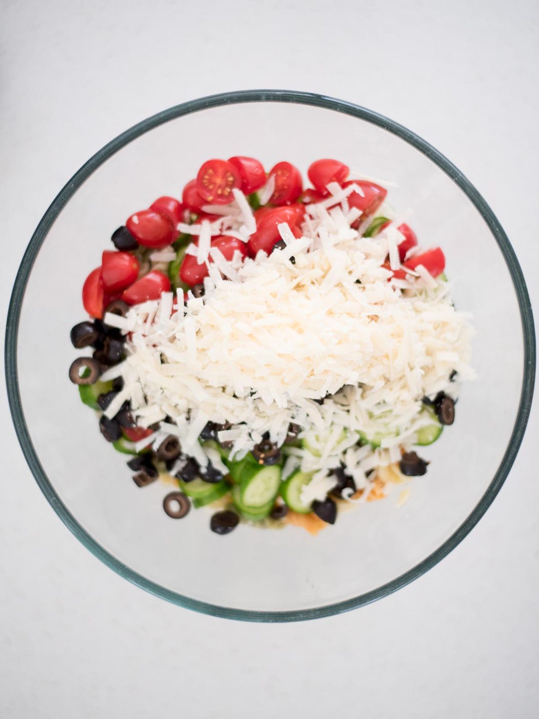 parmesan cheese added to the mixing bowl with vegetables, olives, and cooked pasta