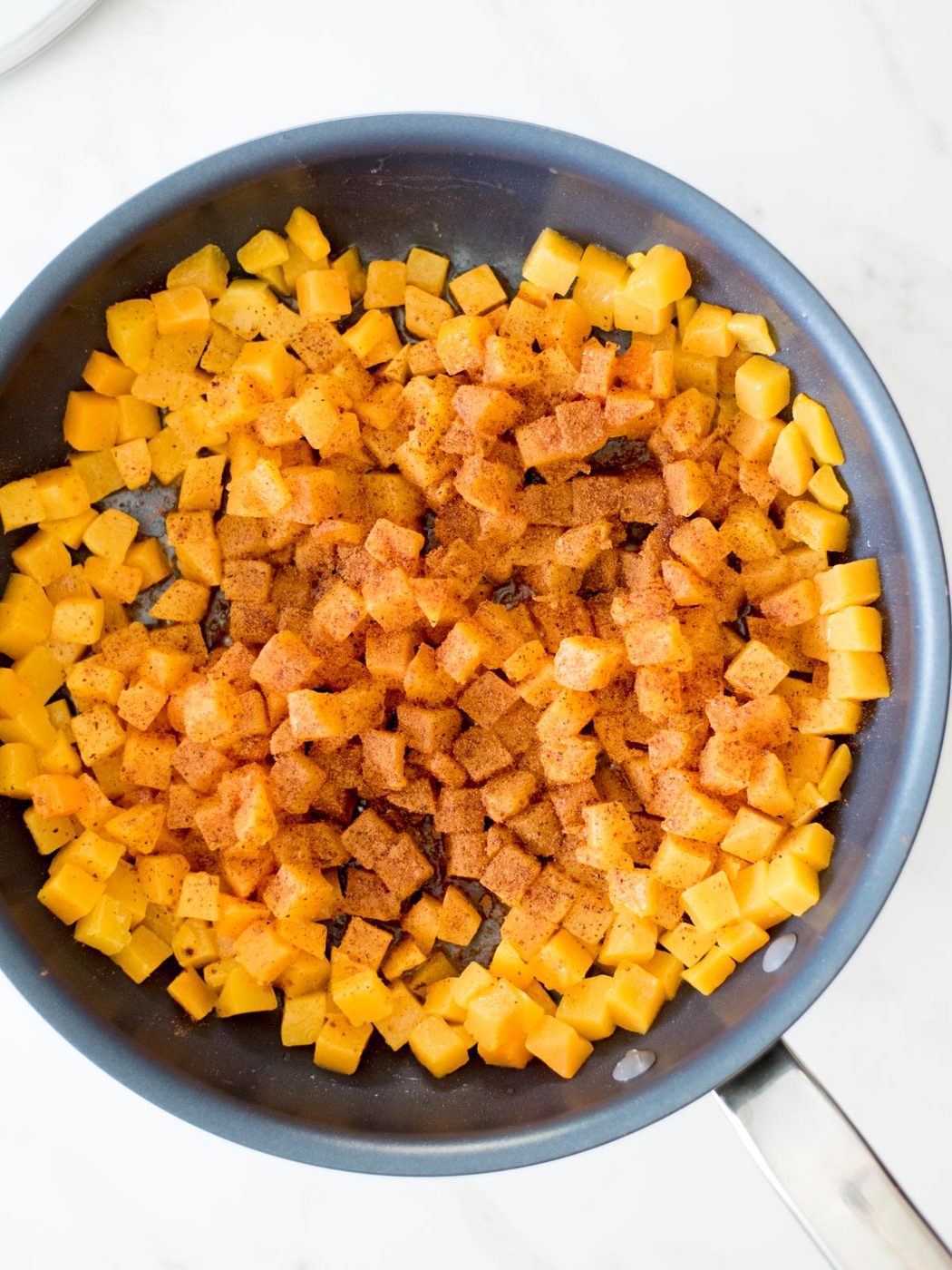 cinnamon and nutmeg sprinkled on butternut squash in a skillet