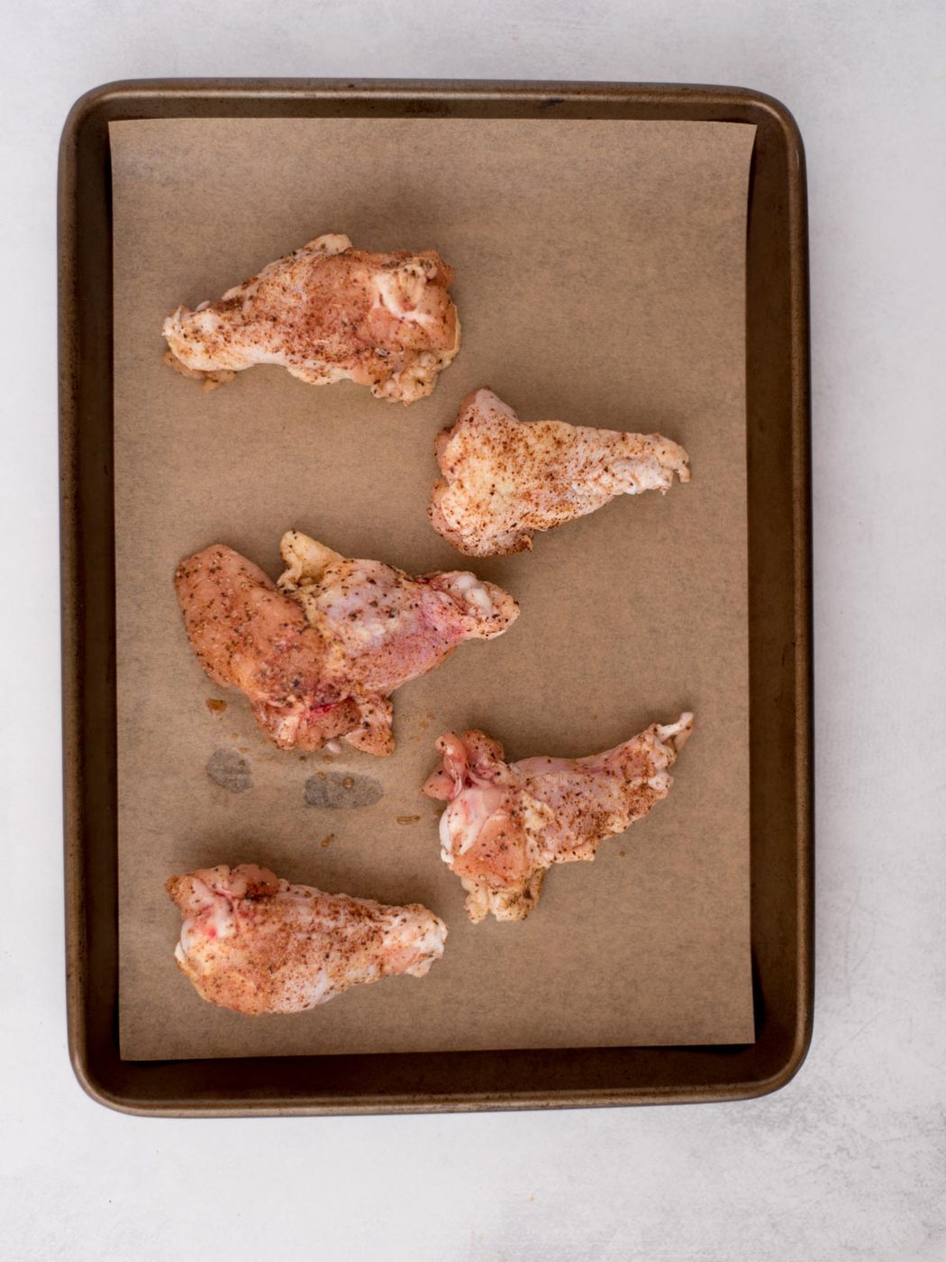 Seasoned raw chicken wings laying on parchment paper covered baking sheet.