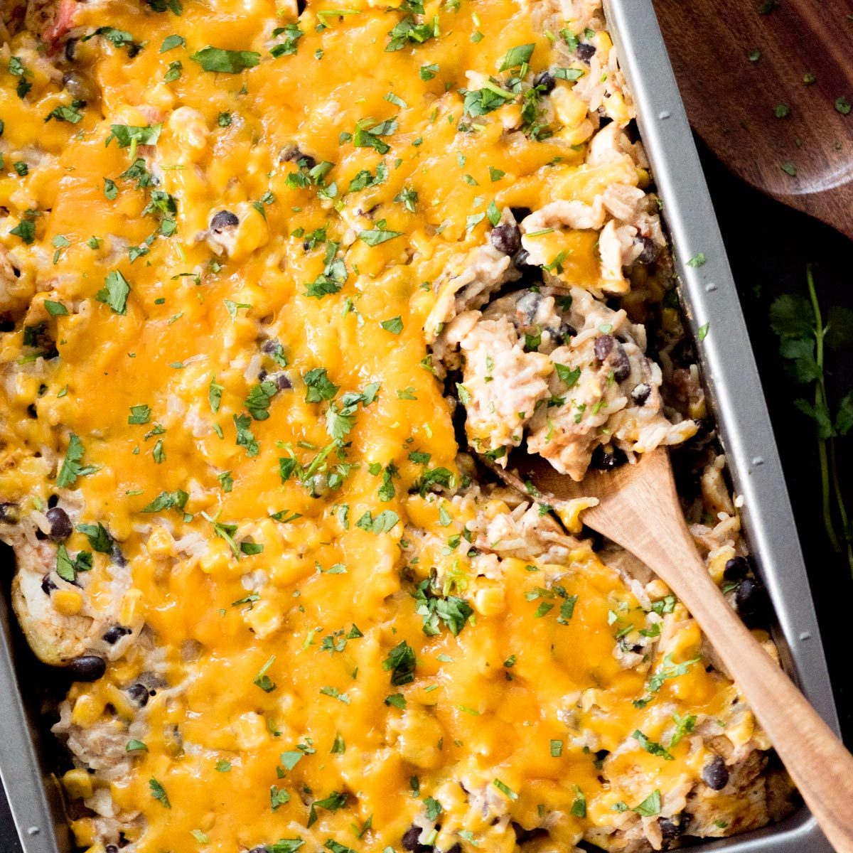 Wooden spoon scooping up a helping of Tex-Mex Chicken with black beans from the baking dish.
